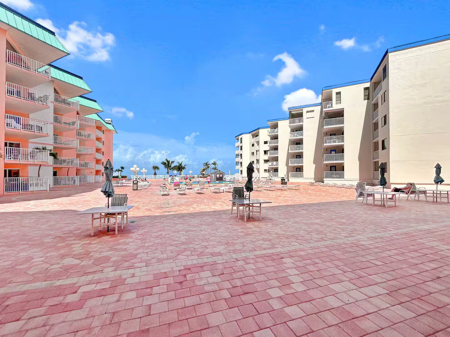 Ein Strandhotel mit mehreren Balkonen, Sitzgelegenheiten im Freien und einem gepflasterten Weg.