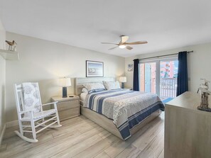 A bedroom with a bed, bedside tables, a rocking chair, a ceiling fan, and a view of the outside. - Ocean-View Oasis: 2BR Condo w/ Pool & Private Balcony (Indian Shores)
