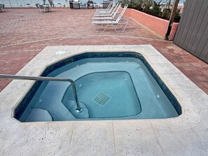 A swimming pool with a metal ladder, surrounded by a brick patio and lounge chairs. - Ocean-View Oasis: 2BR Condo w/ Pool & Private Balcony (Indian Shores)