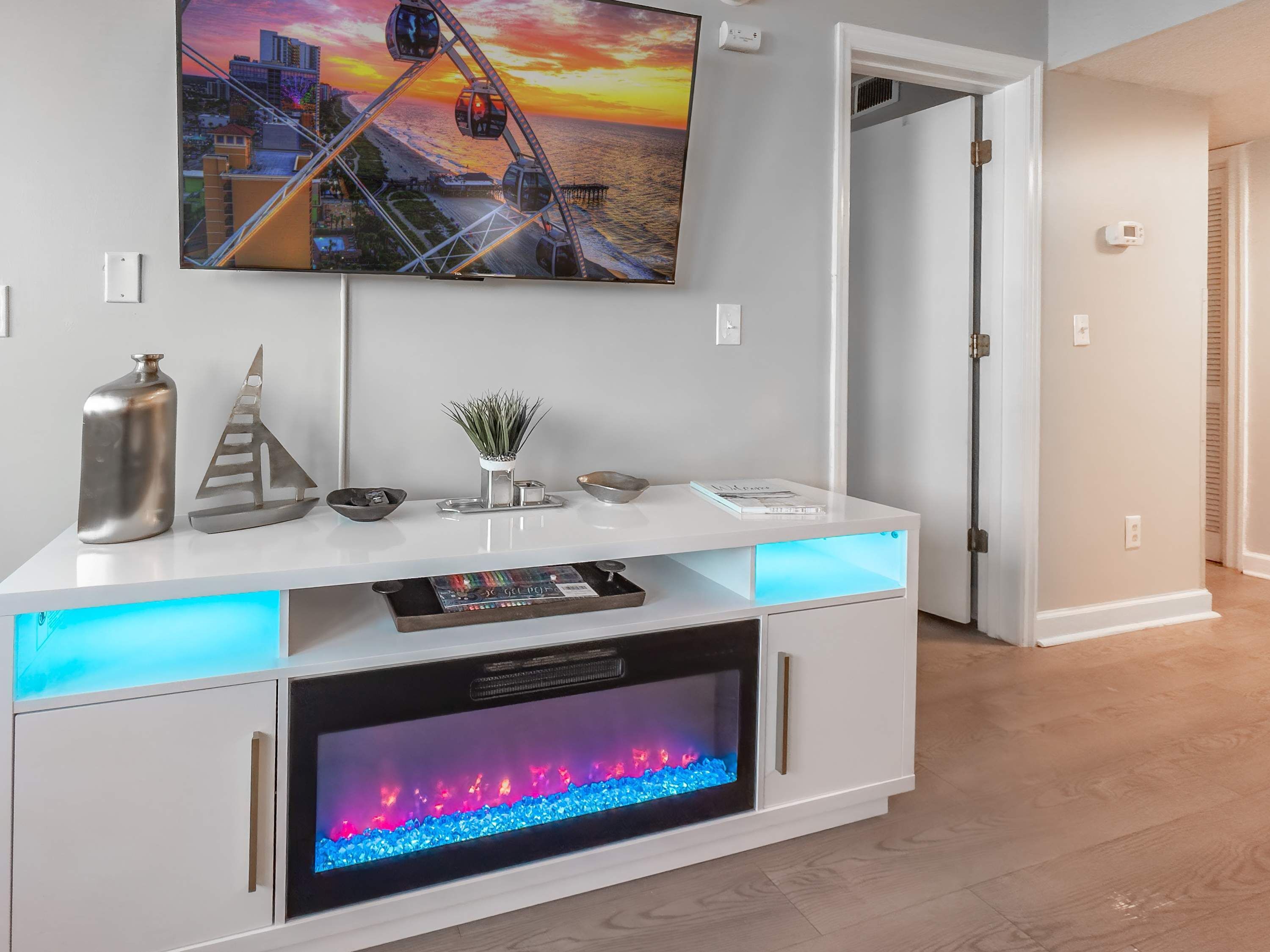A modern living room with a white entertainment unit, a large flat-screen TV, and a built-in fireplace.