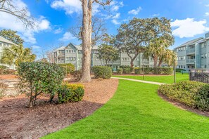 A residential building with a well-maintained lawn, trees, and a clear sky. - Myrtle Beach Resort Five Seasons Unit 4302 (Myrtle Beach)