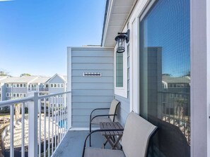 Ein Balkon mit Blick auf andere Gebäude, ein kleiner Tisch, zwei Stühle und ein Fenster mit Fliegengitter.