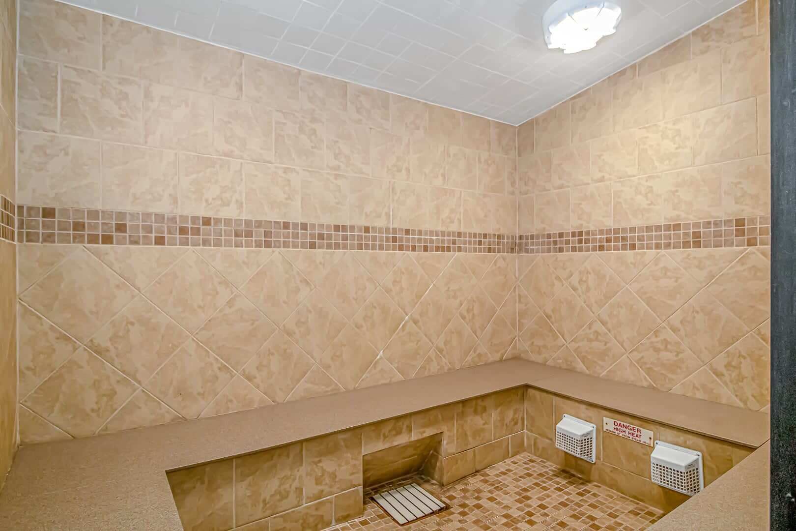 A bathroom with beige tiles, a tiled bench, a shower drain, and a warning sign for high heat.