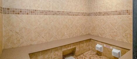 A bathroom with beige tiles, a tiled bench, a shower drain, and a warning sign for high heat.