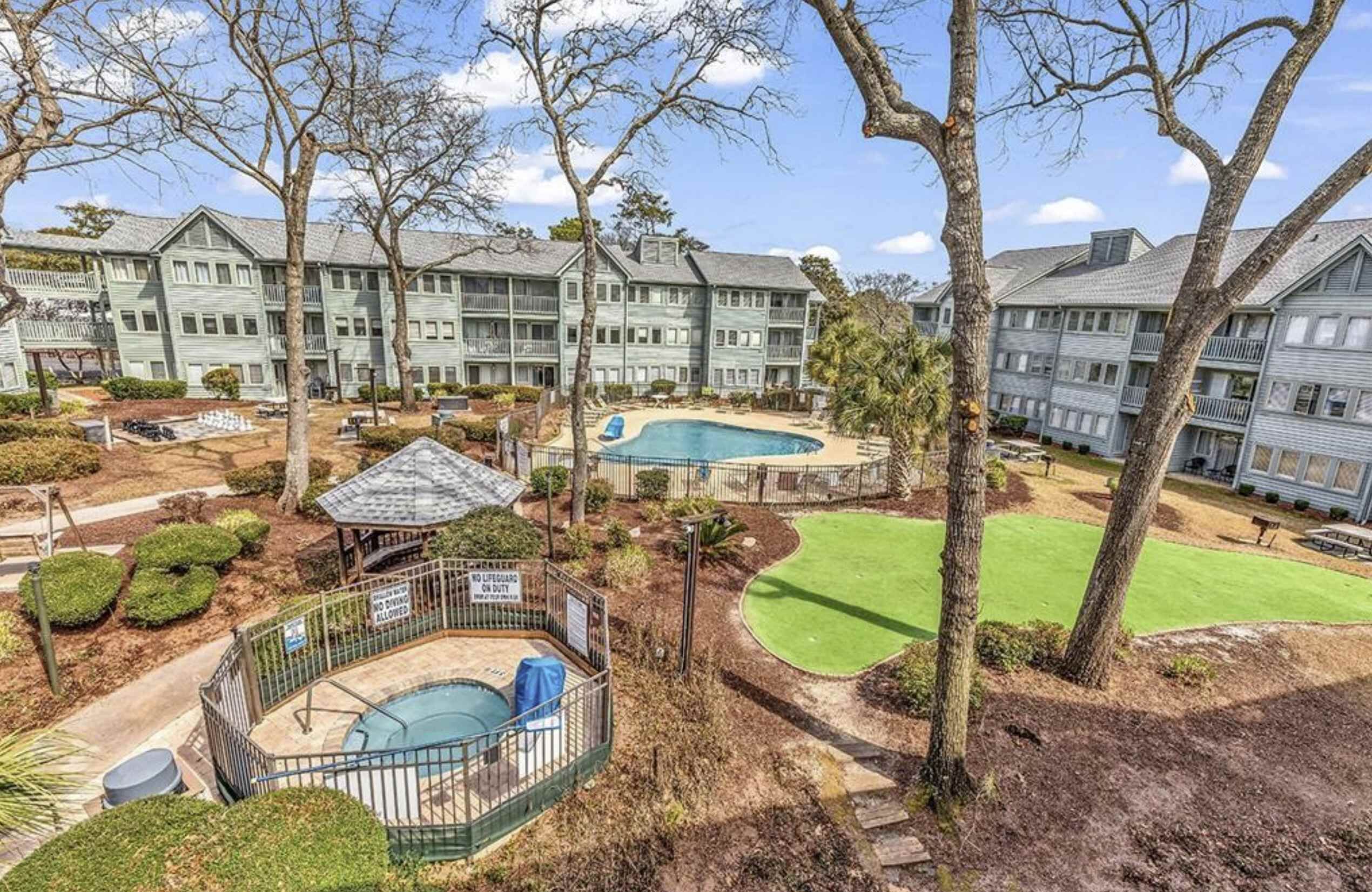 A residential complex with multiple buildings, a swimming pool, and a fenced area with a gazebo.