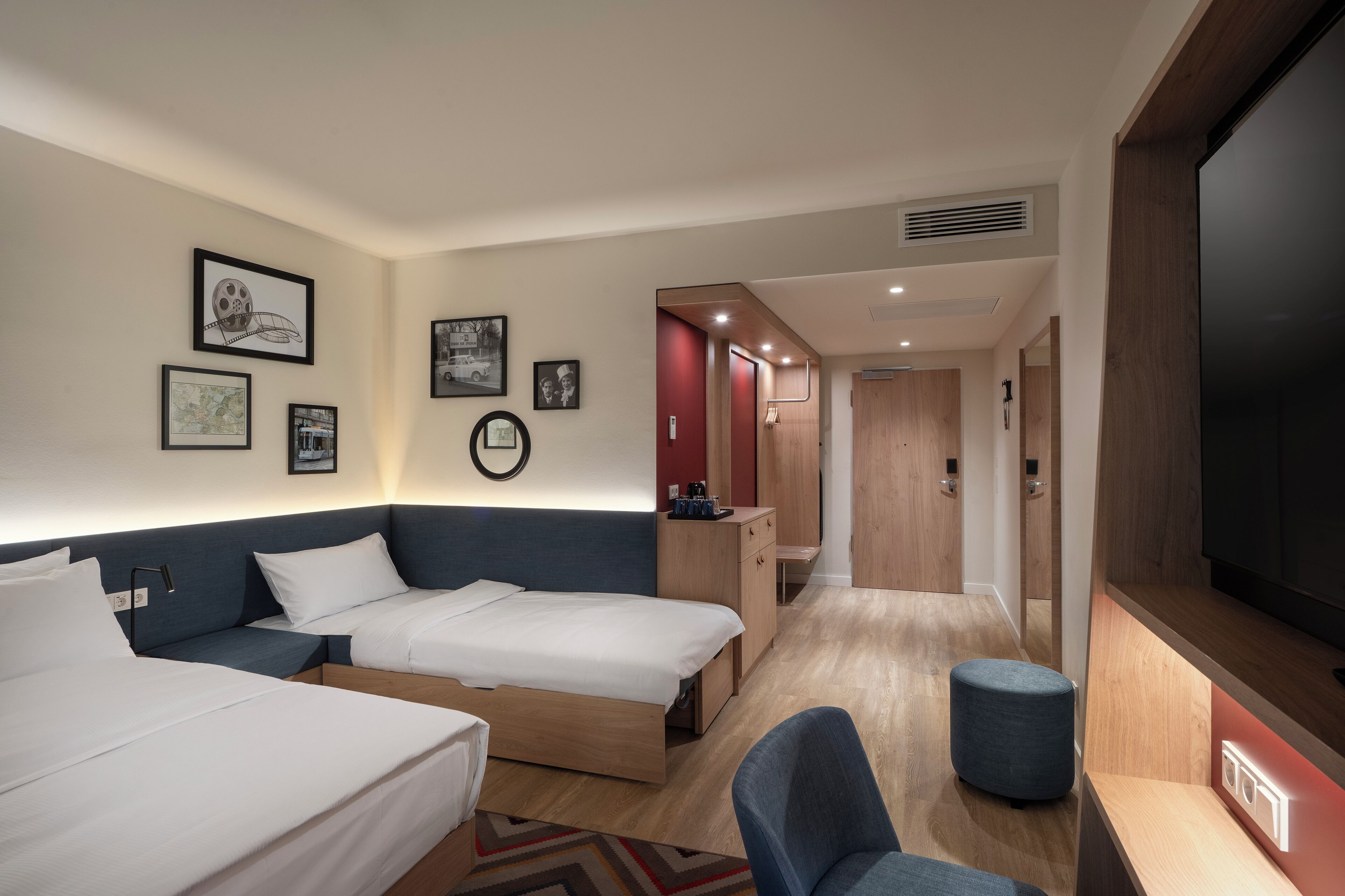 Ein Hotelzimmer mit zwei Betten, einem Schreibtisch, einem Stuhl, einem Fernseher und Bildern an den Wänden.