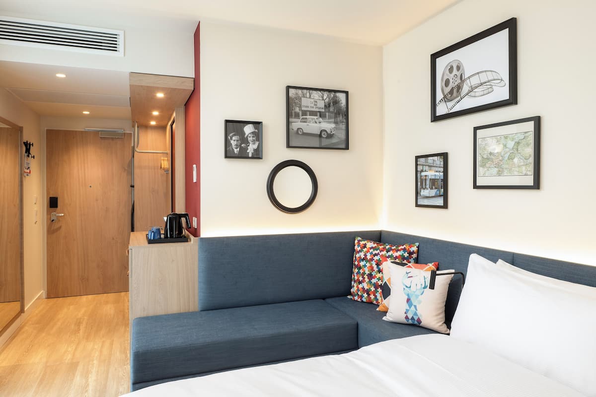 Una habitación de hotel moderna con un sofá azul, una cama y varias fotografías enmarcadas en la pared.