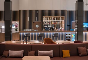 A modern bar area with striped walls, a counter with various bottles, and seating with a sofa and chairs.