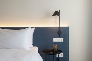 A hotel room with a bed, a nightstand, a lamp, and a wall socket. - Hampton By Hilton Bremen North (Bremen)