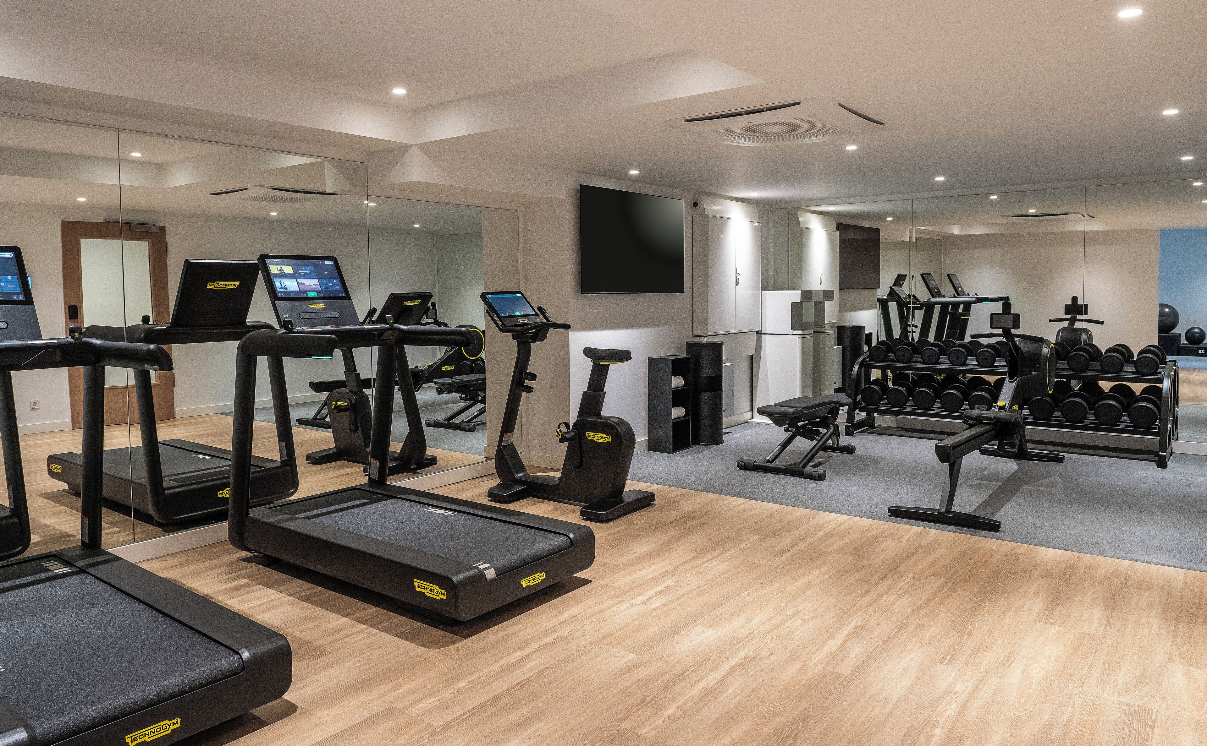 Un gimnasio con cintas de correr, elípticas y un estante con mancuernas.