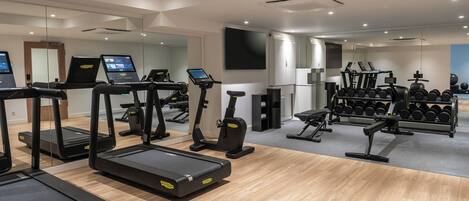 Un gimnasio con cintas de correr, elípticas y un estante con mancuernas.