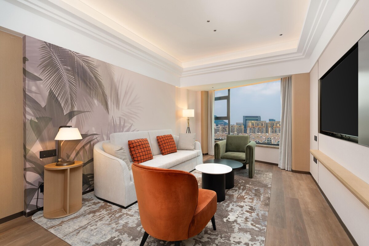 Ein modernes Hotelzimmer mit einer Couch, einem Sessel und einem Flachbildfernseher.