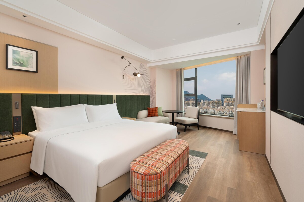 Habitación de hotel con una cama grande, un escritorio, una silla, una mesita y un televisor.