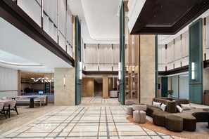 Eine großzügige Lobby mit kariertem Boden, Sitzbereichen, einer Rezeption und einer Bar.