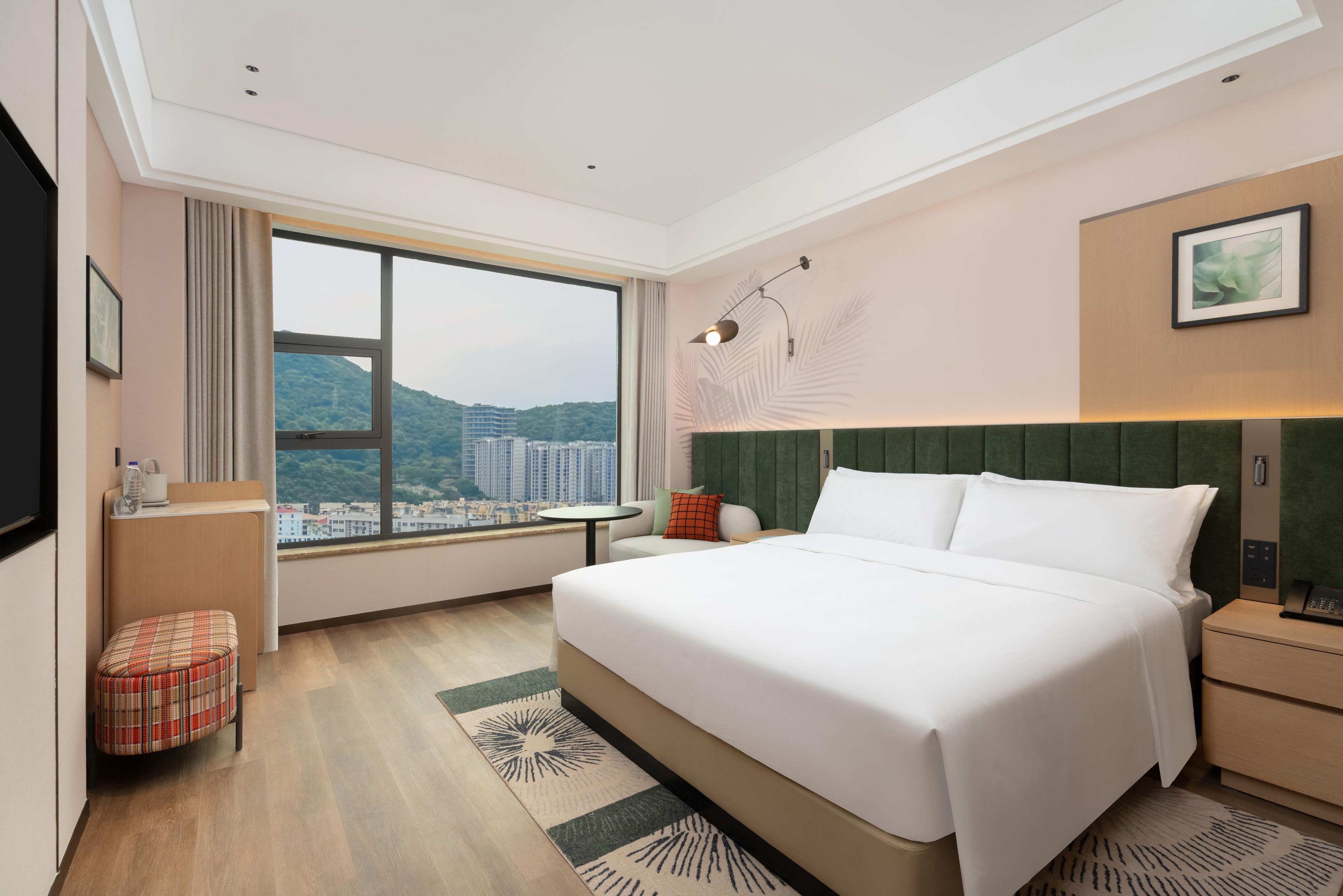 A modern hotel room with a large bed, a view of the city, and a small seating area.