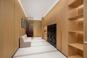 Un moderno cuarto de lavandería con sofá, lavadoras y armarios de madera.