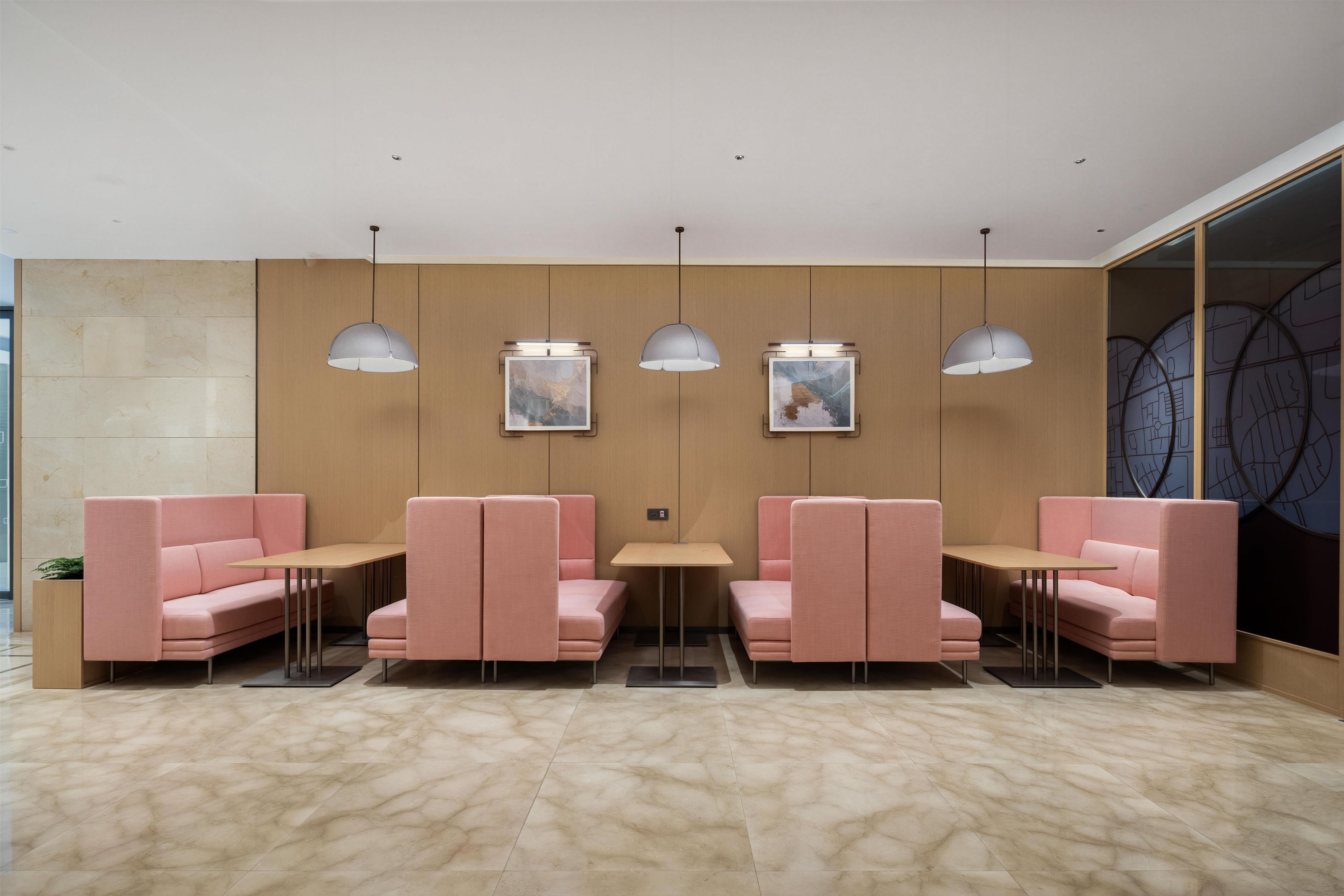 A modern waiting area with pink seating, pendant lighting, and artwork on the walls.