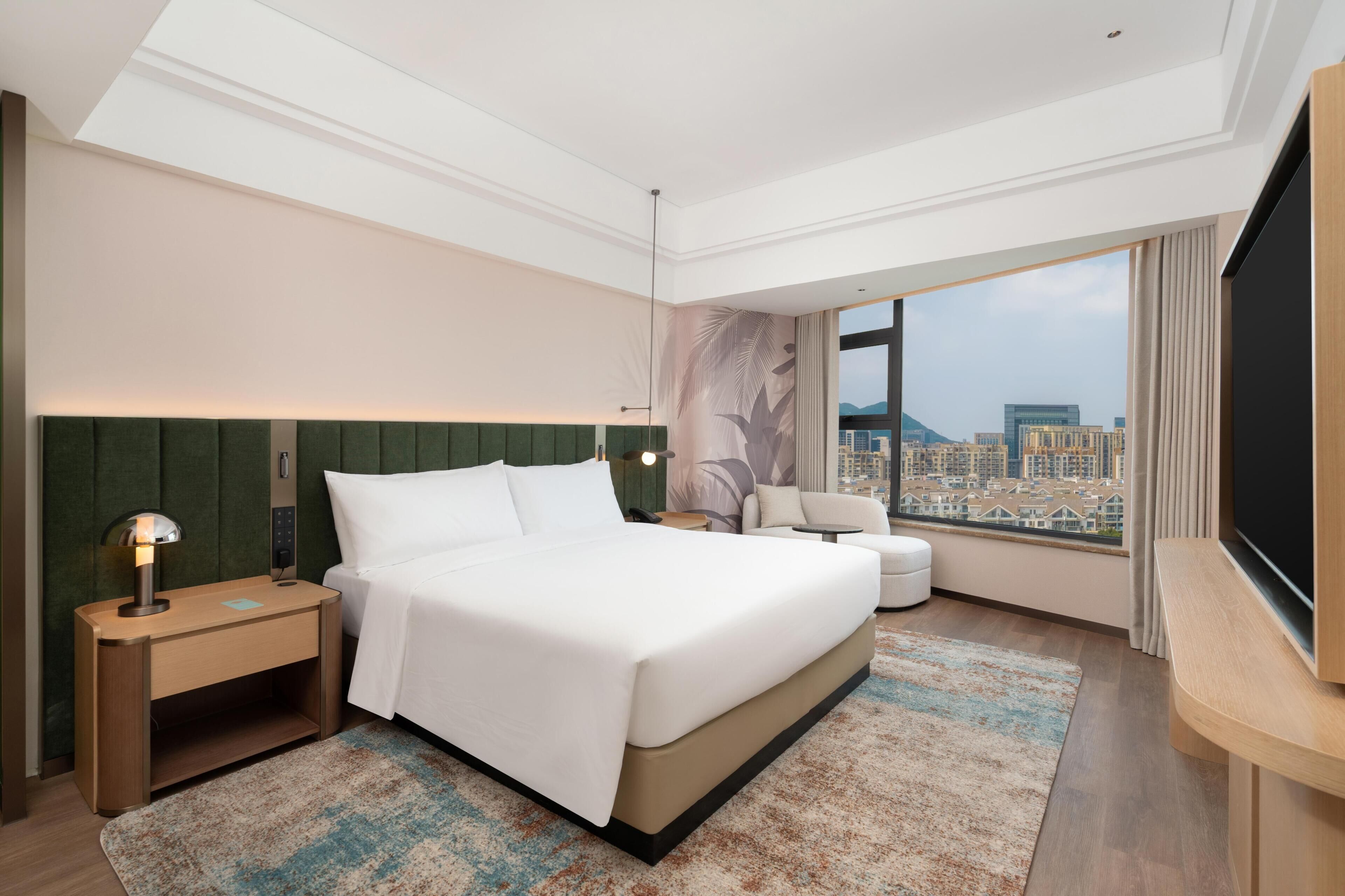 Une chambre d’hôtel moderne dotée d’un grand lit, d’un coin salon, d’une télévision et offrant une vue sur la ville.