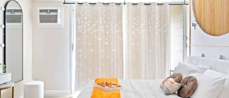 Une chambre à coucher avec un lit, une table de chevet, un miroir et une fenêtre avec des rideaux.