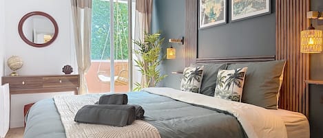 A bedroom with a bed, a dresser, a mirror, and a view of the outdoors.