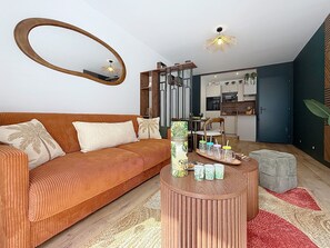 A modern living room with a sofa, a coffee table, a round mirror, and a kitchen in the background. - Love of the Islands • Center • Beach • Parking (Cabourg)