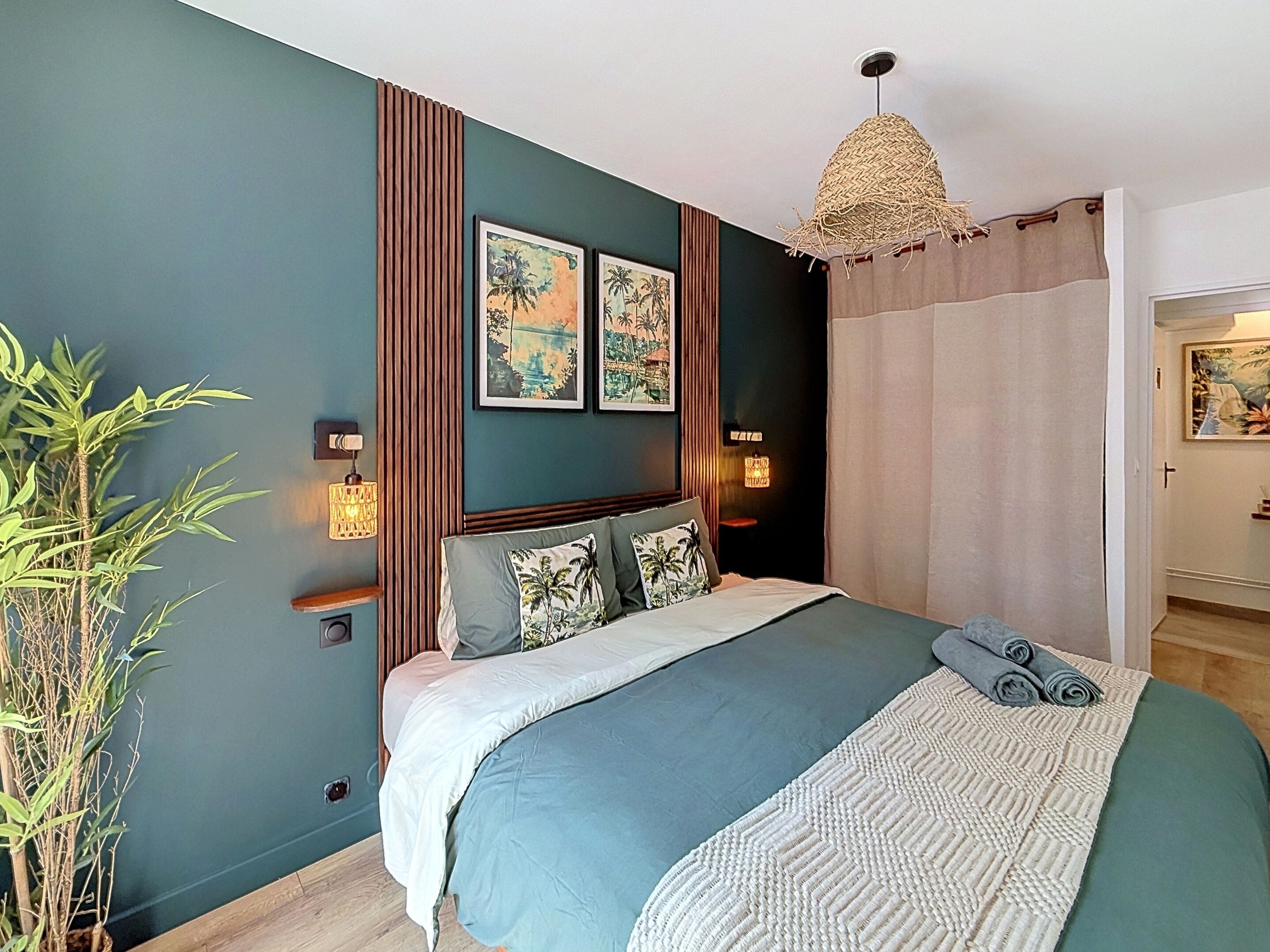 A bedroom with a bed, wall-mounted lights, a hanging light fixture, and a door leading to another room.