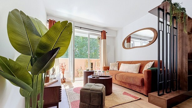 Un salon comprenant un canapé, un pouf, une table basse et une grande plante.
