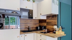 Une cuisine moderne avec des meubles blancs, un mur d’accent en bois, un four à micro-ondes encastré, une machine à café et un petit plan de travail sur lequel se trouve une boîte de biscuits.