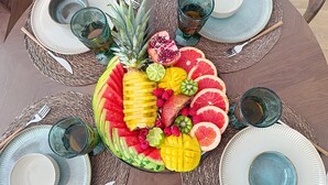 Une table ronde ornée d’un centre de table composé de fruits, avec des assiettes, des couverts et des verres.