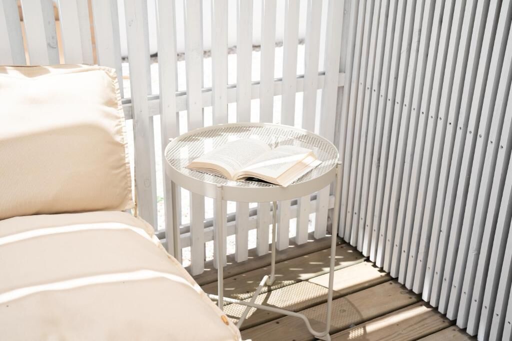 Ein heller Sitzbereich im Freien mit gepolstertem Sessel und kleinem Rundtisch mit offenem Buch.