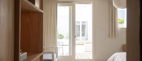 Un dormitorio con cama, armario de madera, puerta corrediza de vidrio que da a un espacio exterior y ventilador de techo.