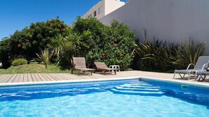 A swimming pool with lounge chairs, surrounded by greenery and a modern building. - Vitaminas - Casa de Playa y Cafe (Punta del Este)
