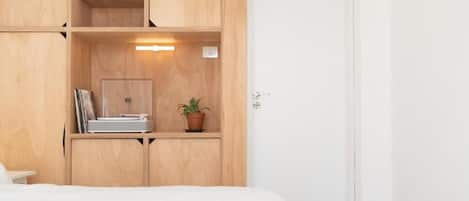 Quarto com cama, guarda-roupa de madeira, prateleiras, uma planta em vaso e mesa de cabeceira.