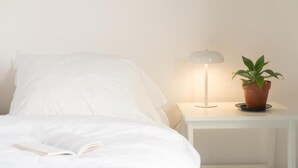 A neatly made bed with a book, a white bedside table with a lamp, and a potted plant. - Vitaminas - Casa de Playa y Cafe (Punta del Este)