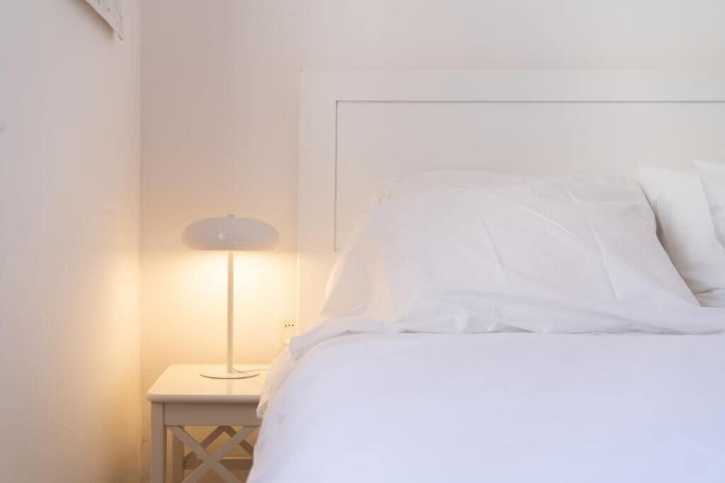 A bed with white bedding and a bedside table with a lamp.