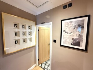 Um corredor com obras de arte emolduradas nas paredes, uma porta de madeira e ladrilhos com padrão.