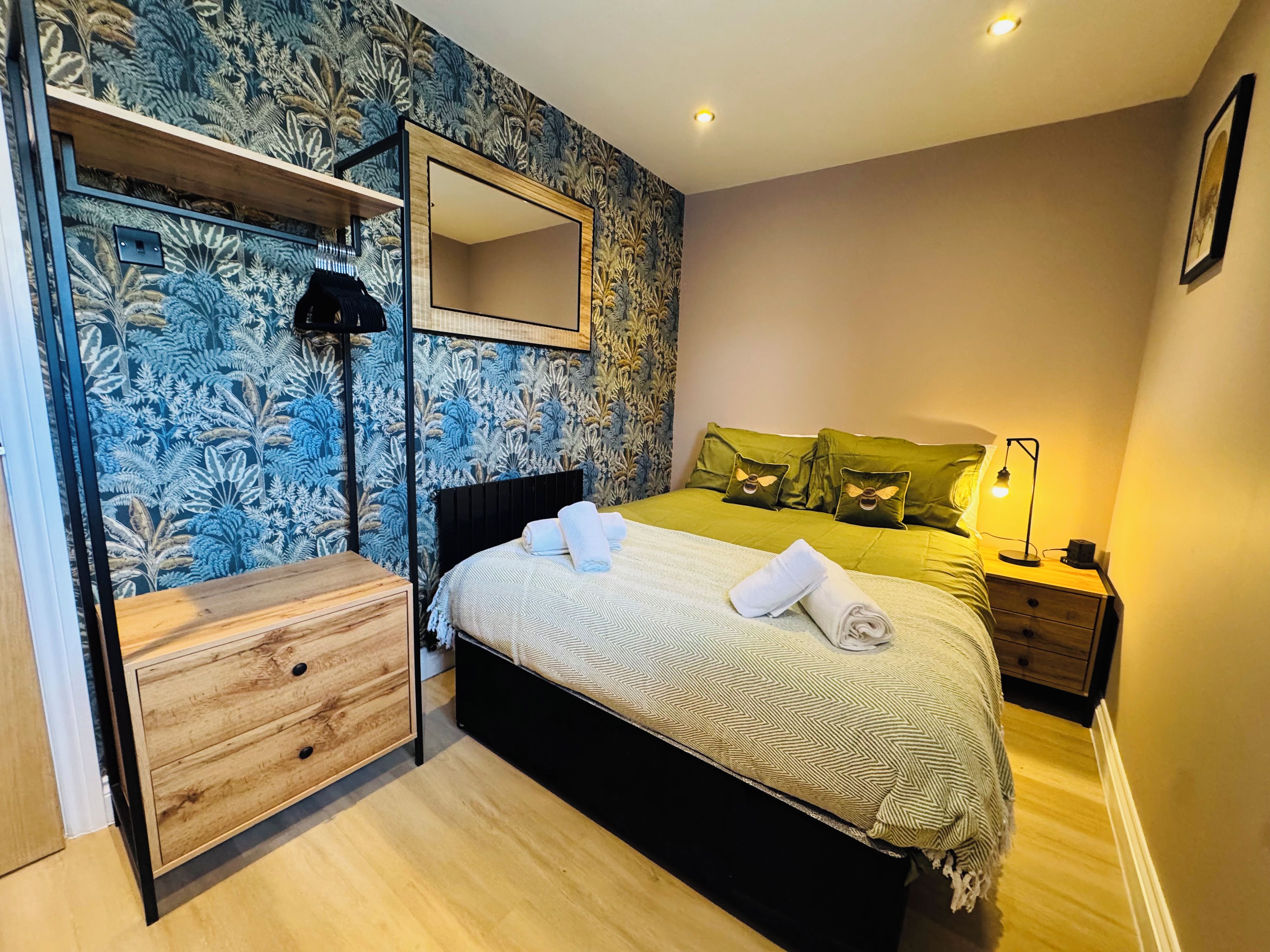 A bedroom with a bed, bedside table, lamp, and a mirror on the wall.