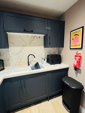 A kitchen with dark cabinets, a marble backsplash, a sink, a toaster, and a fire blanket on the wall. - Station House Flat 4 | 2 Bedrooms | Free Parking | Nintendo Switch (Harrington)