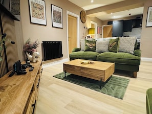 A living room with a green sofa, a wooden coffee table, and a fireplace. - Station House Flat 4 | 2 Bedrooms | Free Parking | Nintendo Switch (Harrington)