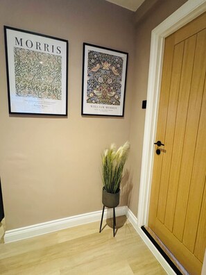 A hallway with two framed artworks on the wall, a potted plant, and a wooden door. - Station House Flat 4 | 2 Bedrooms | Free Parking | Nintendo Switch (Harrington)