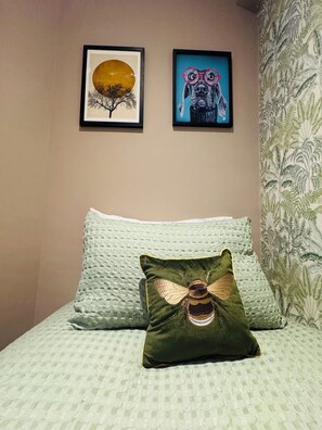 A bed with a textured green blanket and a decorative pillow with a bee design. Two framed artworks are hung on the wall above the bed. - Station House Flat 4 | 2 Bedrooms | Free Parking | Nintendo Switch (Harrington)