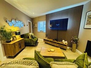 A modern living room with a flat-screen TV, green sofas, a wooden coffee table, and a potted plant. - Station House Flat 4 | 2 Bedrooms | Free Parking | Nintendo Switch (Harrington)