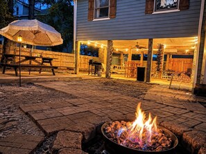 Ein Garten mit Feuerstelle, überdachter Terrasse und Holzzaun.