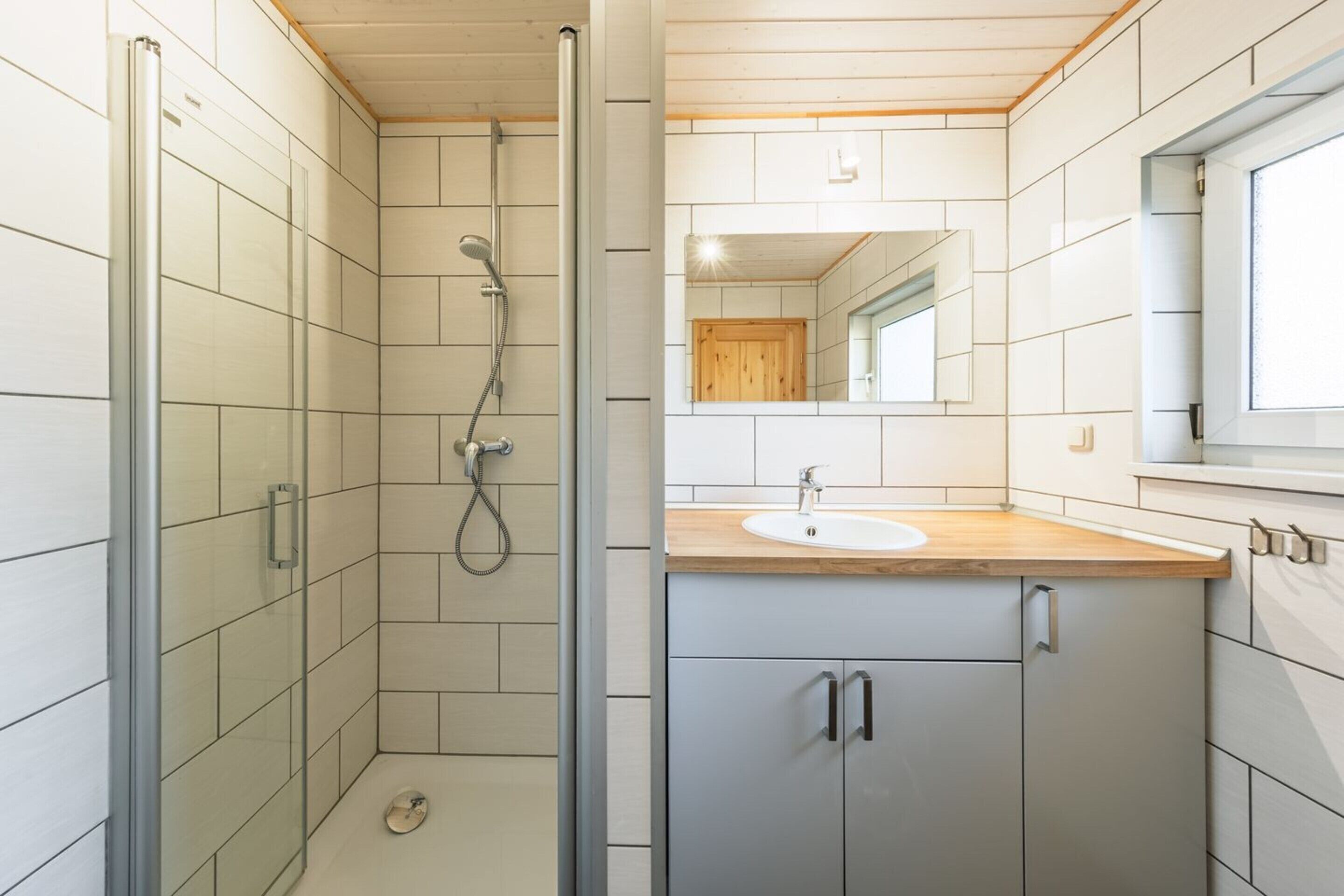 A modern bathroom with a glass shower enclosure, a wooden vanity with a sink, and a mirror above the vanity.