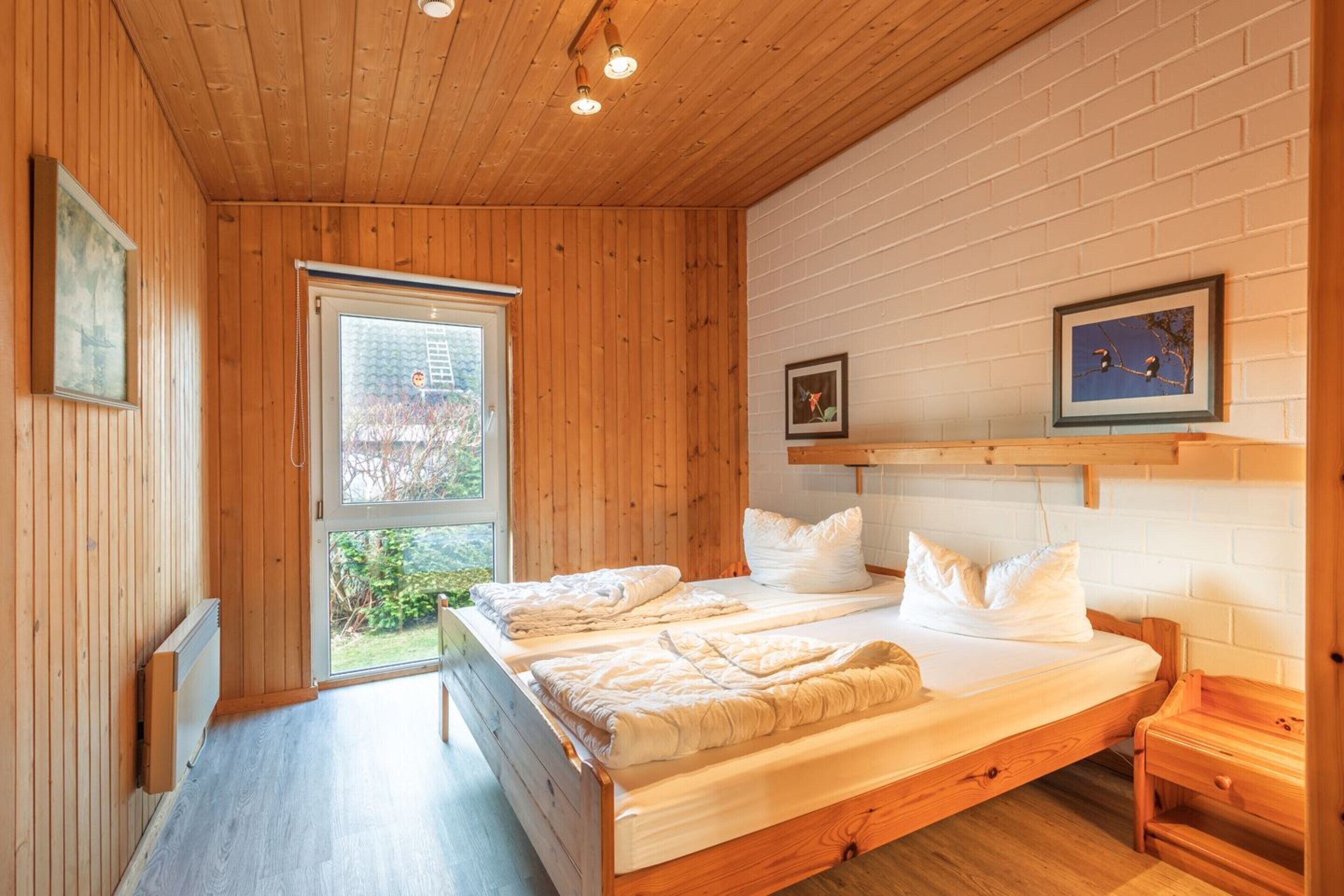 A bedroom with two beds, a window, and a wooden ceiling.