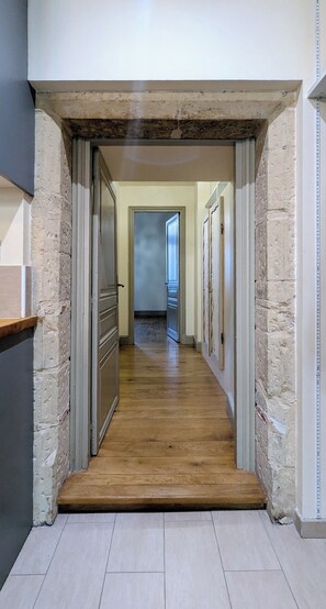 A hallway with wooden flooring, white walls, and a door leading to another room.
