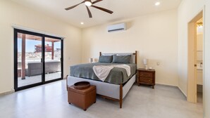 Ein Schlafzimmer mit Bett, Nachttischen, Deckenventilator, Klimaanlage und einer Schiebetür zu einem Außenbereich.