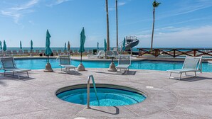 Ein Poolbereich mit Liegestühlen und Sonnenschirmen, einem Whirlpool und Blick auf den Ozean.