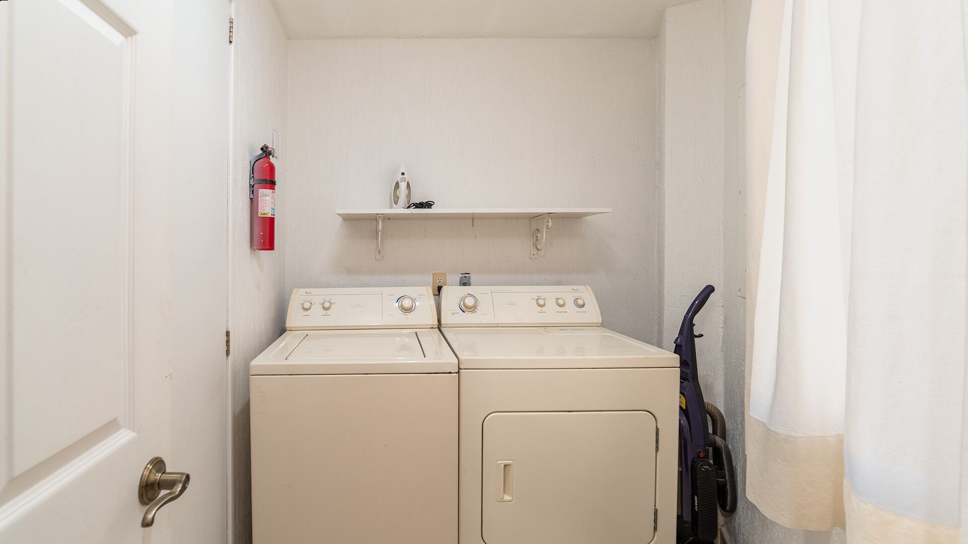 A laundry room with two washing machines, a fire extinguisher, and a shelf above the machines.