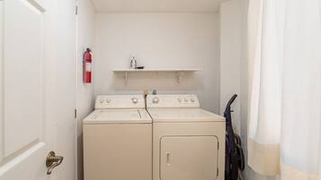 A laundry room with two washing machines, a fire extinguisher, and a shelf above the machines.
